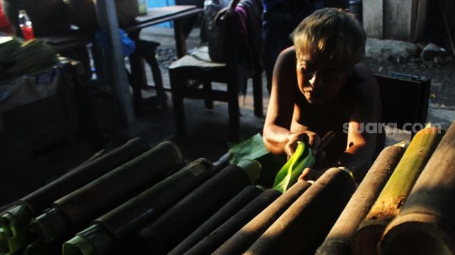 Pembuat nasi lemang memasukan daun pisang ke dalam bambu, di kawasan Senen, Jakarta Pusat, Senin (19/4/2021). [Suara.com/Dian Latifah]
