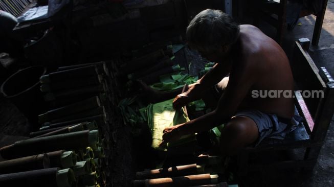 Pekerja menggulung daun pisang yang akan di masukkan ke dalam bambu, di kawasan Senen, Jakarta Pusat, Senin (19/4/2021). [Suara.com/Dian Latifah]