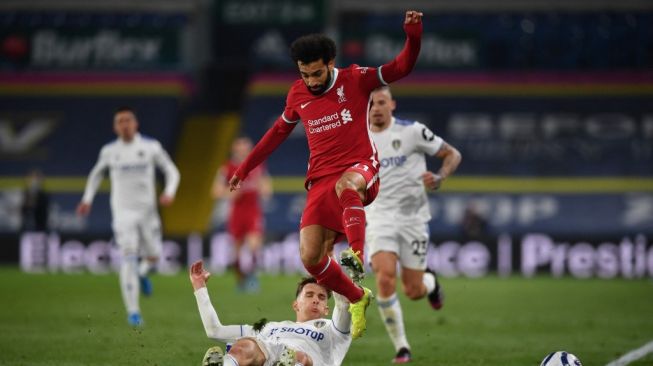 Penyerang Liverpool, Mohamed Salah (baju merah) melompat saat bek Leeds United, Diego Llorente melakukan tekel untuk merebut bola darinya dalam laga pekan ke-32 Liga Inggris, di Ellan Road, Selasa (20/4/2021). [Paul ELLIS / POOL / AFP].