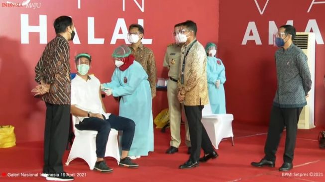 Aktor Nicholas Saputra melakukan vaksinasi Covid-19 di Galeri Nasional Indonesia yang turut disaksikan langsung Presiden Joko Widodo, Senin (19/4/2021). [Tangkapan Layar YouTube Setkab]
