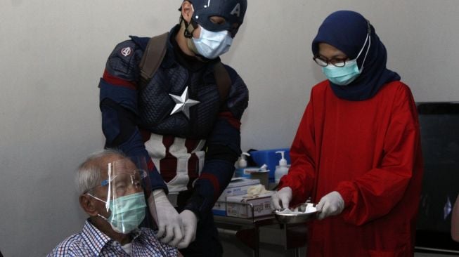 Dokter superhero Rollando Erric Manibuy (tengah) menyuntikkan vaksin COVID-19 dosis kedua kepada lansia berusia 104 tahun Wirjawan Hardjamulia di Rumah Sakit Vania, Kota Bogor, Jawa Barat, Selasa (20/4/2021).
