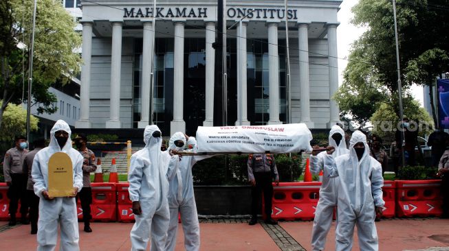 Pendemo membawa replika batu nisan sebagai bagian dari teatrikal yang dilakukan di  Mahkamah Konstitusi, Jakarta Pusat, Rabu (21/4/2021).  [Suara.com/Dian Latifah]   