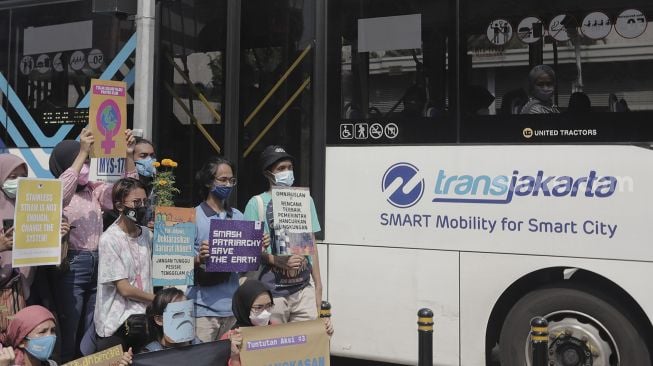 Penumpang bus Transjakarta menyaksikan aktivis lingkungan hidup yang menggelar aksi "Joget Jagat" di Jalan MH Thamrin, Jakarta, Kamis (22/4/2021). [Suara.com/Angga Budhiyanto]