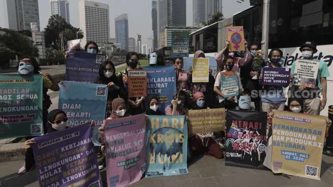 Aktivis lingkungan hidup membentangkan poster saat menggelar aksi "Joget Jagat" di Jalan MH Thamrin, Jakarta, Kamis (22/4/2021). [Suara.com/Angga Budhiyanto]