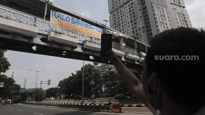 Seorang pendukung Persija mengambil gambar spanduk Persija Jakarta juara Piala Menpora 2021 yang terpasang di kawasan Mampang Prapatan, Jakarta, Senin (26/4/2021). [Suara.com/Angga Budhiyanto]