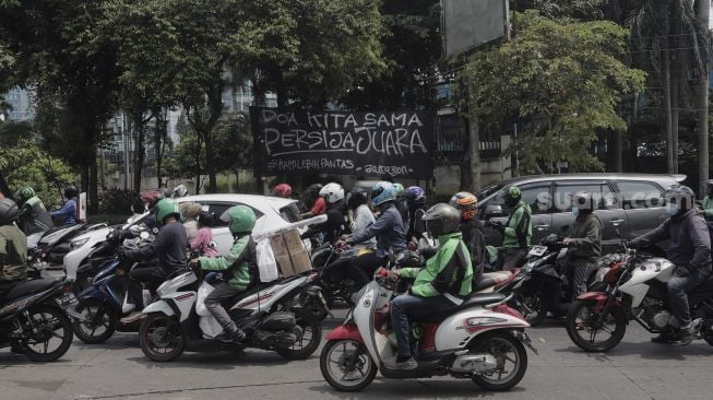 Sejumlah kendaraan melintas di depan spanduk Persija Jakarta juara Piala Menpora 2021 yang terpasang di kawasan Pasar Minggu, Jakarta, Senin (26/4/2021). [Suara.com/Angga Budhiyanto]