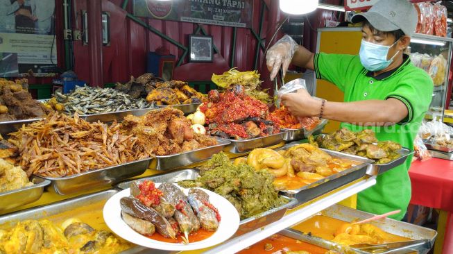 Pedagang nasi kapau melayani pembeli di Food Street Kramat di Kawasan Senen, Jakarta Pusat, Selasa (27/4/2021). [Suara.com/Alfian Winanto]