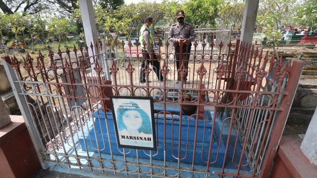 Dua orang anggota polisi berjaga di makam pejuang buruh Marsinah di Desa Nglundo, Nganjuk, Jawa Timur, Sabtu (1/5/2021).  ANTARA FOTO/Prasetia Fauzani
