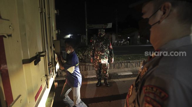 Petugas gabungan memeriksa kendaraan yang melintas di pos penyekatan Tanjungpura saat hari pertama penyekatan larangan mudik di Karawang, Jawa Barat, Kamis (6/5/2021). [Suara.com/Angga Budhiyanto]