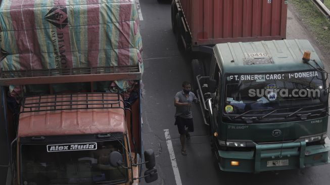 Pengemudi berjalan memasuki truknya saat terjebak kemacetan di jalan Tol Jakarta-Cikampek, Cikarang, Kabupaten Bekasi, Jawa Barat, Kamis (6/5/2021). [Suara.com/Angga Budhiyanto]