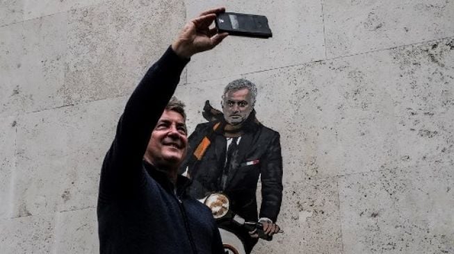 Seorang pria berswafoto di depan mural Jose Mourinho mengendarai Vespa di sebuah tembok kawasan Testaccio, Roma, Jumat (7/5/2021). Andreas SOLARO / AFP