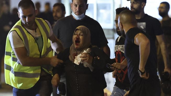 Pengunjuk rasa Palestina membantu seorang perempuan yang terluka di tengah bentrokan dengan pasukan keamanan Israel di Kota Tua Yerusalem, pada (8/5/2021). [EMMANUEL DUNAND / AFP]