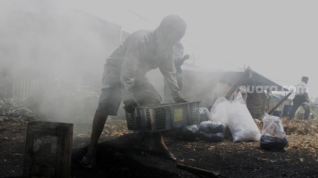 Pekerja mengangkat arang yang sudah jadi di Kawasan Gang Sentiong, Kramat, Jakarta Pusat, Senin (10/5/2021). [Suara.com/Dian Latifah]