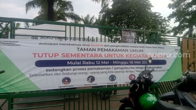 Pengumuman larangan ziarah kubur yang terpasang di gerbang masuk TPU Karet Bivak. (Suara.com/Arga)