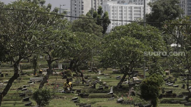 Petugas membersihkan makam di Tempat Pemakaman Umum (TPU) Karet Bivak, Jakarta, Rabu (12/5/2021). [Suara.com/Angga Budhiyanto]