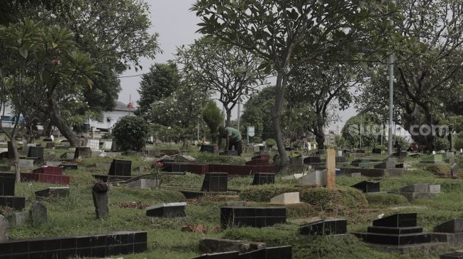 Petugas membersihkan makam di Tempat Pemakaman Umum (TPU) Karet Bivak, Jakarta, Rabu (12/5/2021). [Suara.com/Angga Budhiyanto]