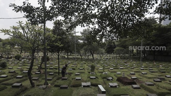 Petugas membersihkan makam di Tempat Pemakaman Umum (TPU) Karet Bivak, Jakarta, Rabu (12/5/2021). [Suara.com/Angga Budhiyanto]