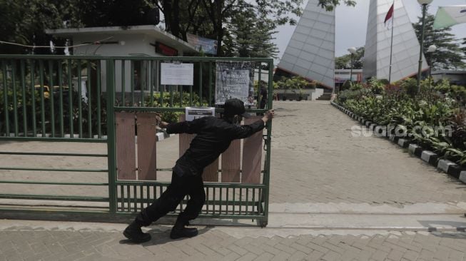 Petugas keamanan menutup pintu masuk ke Tempat Pemakaman Umum (TPU) Karet Bivak, Jakarta, Rabu (12/5/2021). [Suara.com/Angga Budhiyanto]