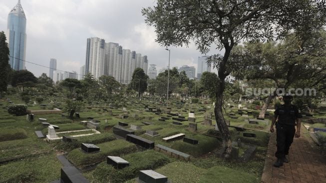 Petugas keamanan berjaga di area makam di Tempat Pemakaman Umum (TPU) Karet Bivak, Jakarta, Rabu (12/5/2021). [Suara.com/Angga Budhiyanto]