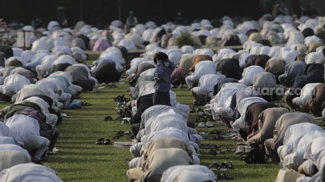 Seorang anak berdiri saat sejumlah umat Muslim menunaikan ibadah Salat Idul Fitri 1442 H di lingkungan Masjid Al-Azhar, Jakarta, Kamis (13/5/2021). [Suara.com/Angga Budhiyanto]