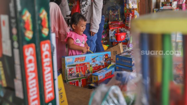 Seorang bocah tersenyum saat membeli mainan di Pasar Gembrong, Jakarta Timur, Jumat (14/5/2021). [Suara.com/Alfian Winanto]