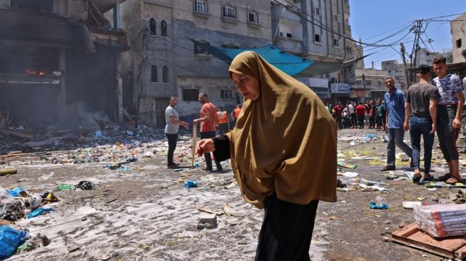 Seorang perempuan Palestina berjalan di antara puing-puing bangunan di Rafah, Jalur Gaza pada 15 Mei 2021. Gaza telah dibom Israel selama beberapa hari terakhir. [AFP/Said Khatib]
