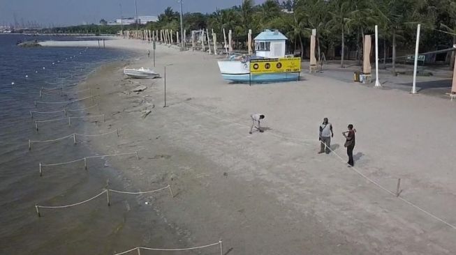 Petugas memasang tali pancang untuk membatasi area pantai dengan laut di kawasan Taman Impian Jaya Ancol, Jakarta Utara, Sabtu (15/5/2021). (Antara/ HO-Taman Impian Jaya Ancol)