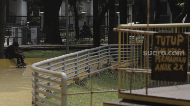 Seorang anak beristirahat di sela-sela bermain papan seluncur (skateboard) di Taman Puring, Kebayoran Baru, Jakarta, Minggu (16/5/2021). [Suara.com/Angga Budhiyanto]
