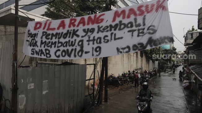 Pengendara melintas di dekat spanduk peringatan untuk pemudik di Jalan Pancoran Barat XI, Jakarta, Senin (17/5/2021). [Suara.com/Angga Budhiyanto]