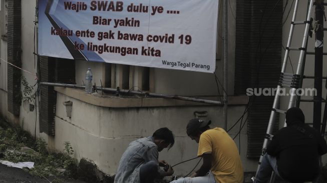 Pekerja memperbaiki instalasi kabel di dekat spanduk peringatan untuk pemudik di kawasan Tegal Parang, Jakarta, Senin (17/5/2021). [Suara.com/Angga Budhiyanto]