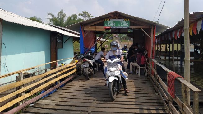 Pengendara melintasi jembatan kayu milik perorangan di Waduk Saguling, Kabupaten Bandung Barat. [Suara.com/Ferrye Bangkit Rizki]