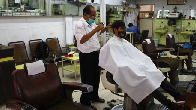 Pemangkas rambut Sukadi memotong rambut seorang pelanggannya di gerai pangkas rambut Sahabat di komplek pertokoan Kayutangan Heritage, Malang, Jawa Timur, Senin (17/5/2021). ANTARA FOTO/Ari Bowo Sucipto