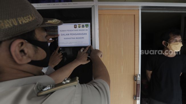 Lurah Lenteng Agung, Bayu Pasca memasangkan stiker tanda menjalani isolasi mandiri pada rumah pemudik yang baru kembali ke Jakarta di kawasan Lenteng Agung, Jakarta, Senin (17/5/2021). [Suara.com/Angga Budhiyanto]