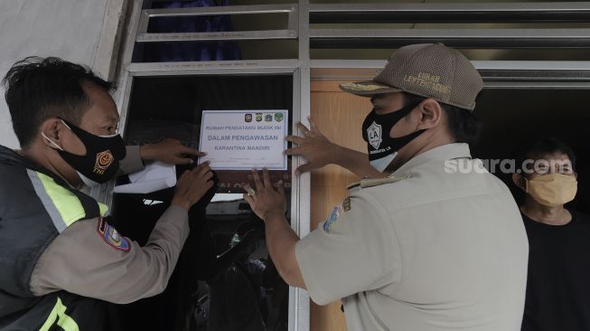 Lurah Lenteng Agung, Bayu Pasca (tengah) memasangkan stiker tanda menjalani isolasi mandiri pada rumah pemudik yang baru kembali ke Jakarta di kawasan Lenteng Agung, Jakarta, Senin (17/5/2021). [Suara.com/Angga Budhiyanto]