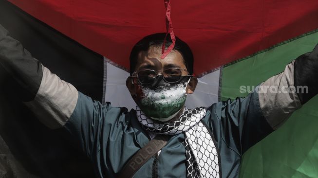 Seorang massa aksi membawa bendera Palestina saat mengikuti aksi solidaritas dukung Palestina terkait kekerasan yang terjadi beberapa waktu lalu oleh Israel di depan Kedubes AS, Jakarta, Selasa (18/5/2021). [Suara.com/Angga Budhiyanto]