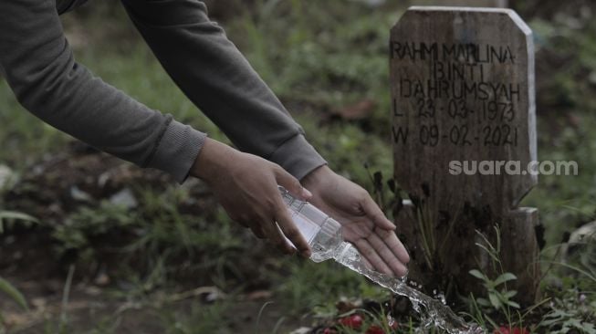 Warga menyiramkan air ke makam keluarganya saat melakukan ziarah kubur di pemakaman khusus COVID-19 di TPU Srengseng Sawah, Jakarta, Selasa (18/5/2021). [Suara.com/Angga Budhiyanto]