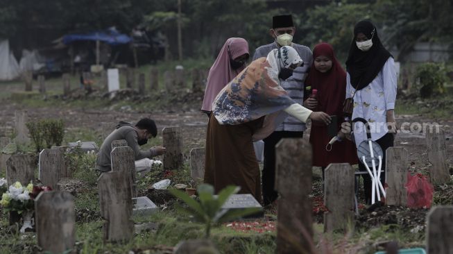 Warga berdoa di makam keluarganya saat melakukan ziarah kubur di pemakaman khusus COVID-19 di TPU Srengseng Sawah, Jakarta, Selasa (18/5/2021). [Suara.com/Angga Budhiyanto]