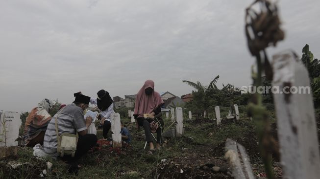 Warga berdoa di makam keluarganya saat melakukan ziarah kubur di pemakaman khusus COVID-19 di TPU Srengseng Sawah, Jakarta, Selasa (18/5/2021). [Suara.com/Angga Budhiyanto]