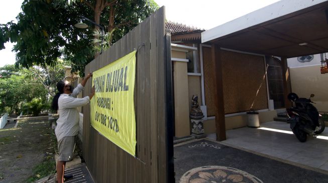 Penjaga memasang spanduk bertuliskan rumah dijual di Perumahan Puri Brawijaya, Banyuwangi, Jawa Timur, Selasa (17/5/2021).  ANTARA FOTO/Budi Candra Setya