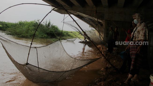 Warga menjaring ikan di Kali Serdang, Bekasi, Selasa (18/5/2021). [Suara.com/Dian Latifah]