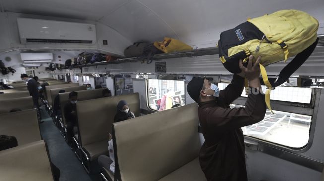 Penumpang meletakkan barang bawaannya saat berada di dalam kereta api yang berhenti di Stasiun Pasar Senen, Jakarta, Rabu (19/5/2021). [Suara.com/Angga Budhiyanto]