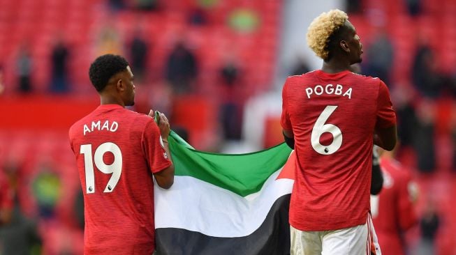 Pemain Manchester United Paul Pogba dan Amad Diallo mengibarkan bendera Palestina usai laga kontra Fulham yang berakhir imbang dalam lanjutan Liga Inggris di Old Trafford, Manchester, Inggris, Selasa (18/5/2021).  Laurence Griffiths / POOL / AFP
