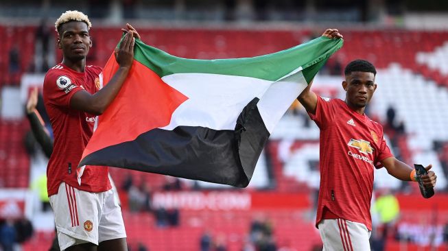 Pemain Manchester United Paul Pogba dan Amad Diallo mengibarkan bendera Palestina usai laga kontra Fulham yang berakhir imbang dalam lanjutan Liga Inggris di Old Trafford, Manchester, Inggris, Selasa (18/5/2021).  Laurence Griffiths / POOL / AFP
