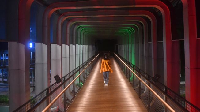 Warga melintasi jembatan penyebrangan orang (JPO) Polda Metro Jaya yang berhias lampu berwarna bendera Palestina di Jakarta, Rabu (19/5/2021). ANTARA FOTO/Akbar Nugroho Gumay
