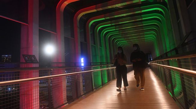 Warga melintasi jembatan penyebrangan orang (JPO) Polda Metro Jaya yang berhias lampu berwarna bendera Palestina di Jakarta, Rabu (19/5/2021). ANTARA FOTO/Akbar Nugroho Gumay
