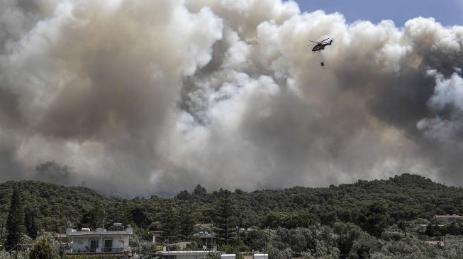 Sebuah helikopter pemadam kebakaran terbang di atas Desa Alepochori, setelah terjadi kebakaran di pegunungan yang menghadap ke Teluk Korintus, pada (20/5/2021). [Louisa GOULIAMAKI / AFP]