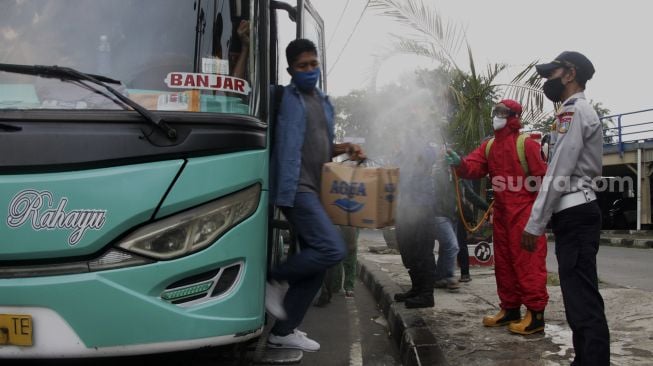 Petugas menyemprotkan cairan disinfektan kepada pemudik yang baru tiba di Terminal Kampung Rambutan, Jakarta, Jumat (21/5/2021). [Suara.com/Dian Latifah]