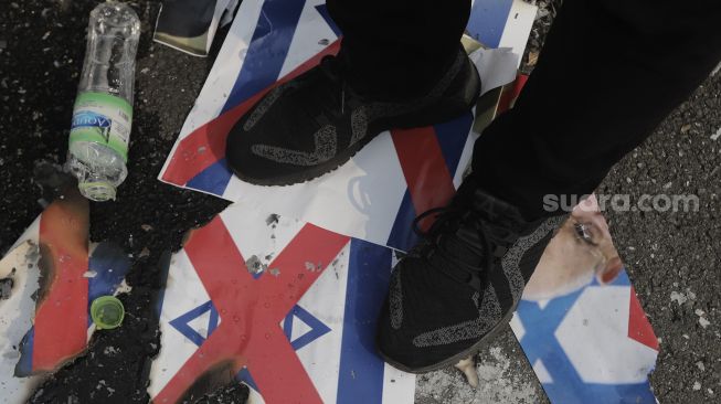 Massa aksi menginjak poster bergambar bendera Israel saat mengikuti aksi solidaritas dukung Palestina terkait kekerasan yang terjadi beberapa waktu lalu oleh Israel di depan Kedubes AS, Jakarta, Jumat (21/5/2021). [Suara.com/Angga Budhiyanto]