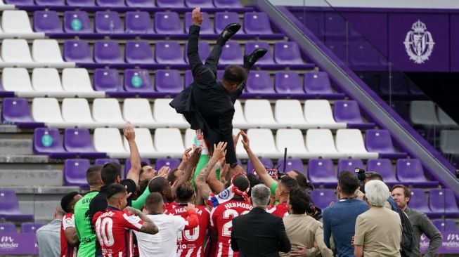 Pelatih Atletico Madrid, Diego Simeone (atas) diangkat oleh para pemain usai Atletico memastikan gelar juara Liga Spanyol 2020/2021 di Estadio Jose Zorilla, Valladolid, Sabtu (22/5/2021) malam WIB. [CESAR MANSO / AFP]