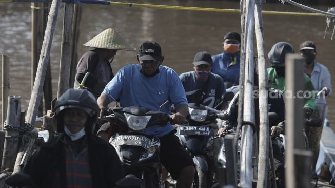 Sejumlah pengendara sepeda motor turun dari perahu eretan usai menyeberangi Kali Cagak, Jakarta Utara, Selasa (25/5/2021). [Suara.com/Angga Budhiyanto]